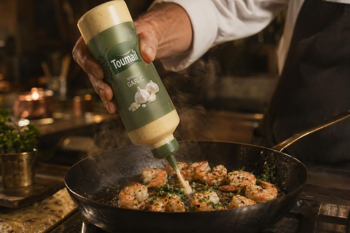 A chef squeezing Toumail Moroccan minced garlic onto a hot pan during service